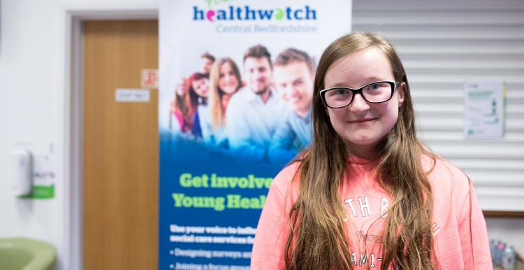 Young girl standing in front of a Healthwatch banner