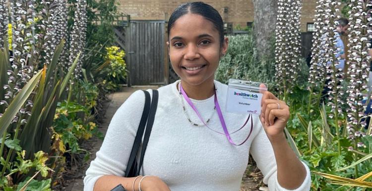 A woman in a white top holding a Healthwatch volunteer badge.