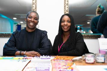 two female staff members sitting behind a desk full of stationary