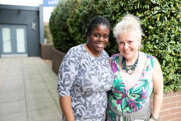 Two women stood in a courtyard with their arms round each other