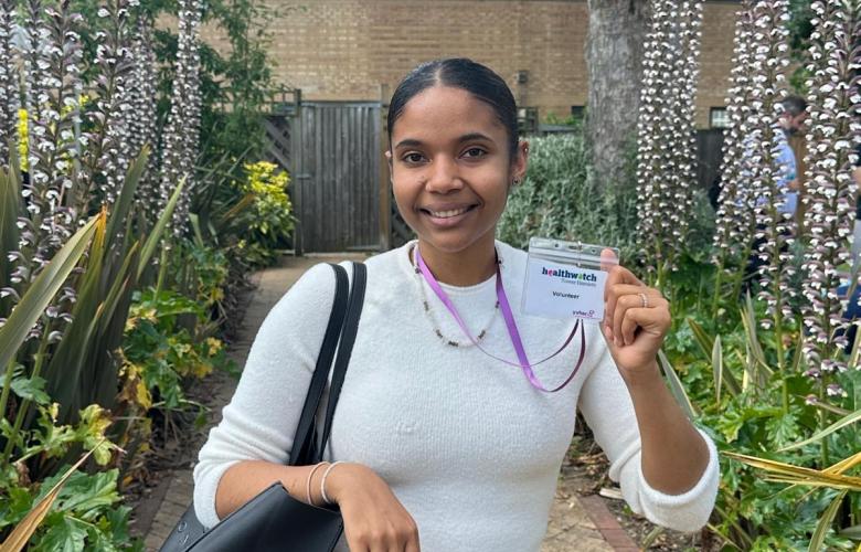 A woman in a white top holding a Healthwatch volunteer badge.