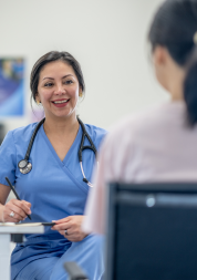 A woman in blue scrubs and wearing a stethoscope smiling at another person.